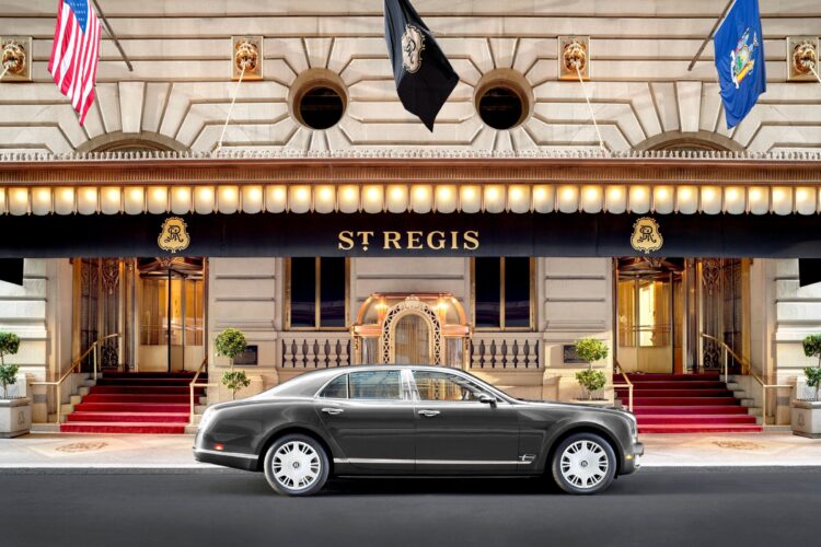 Luxury car parked in front of The St. Regis New York with red carpet entrance and flags