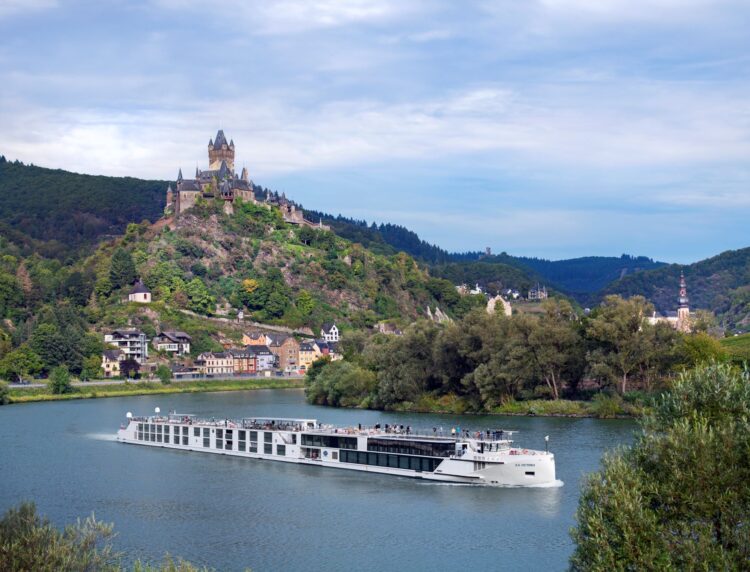 Uniworld luxury river cruise ship sailing through the Moselle River with Cochem Castle in the background