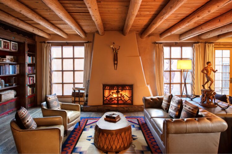 Cozy Southwestern-style hotel lounge with leather chairs, adobe fireplace, wood-beamed ceiling, and Native American-inspired decor in Santa Fe.