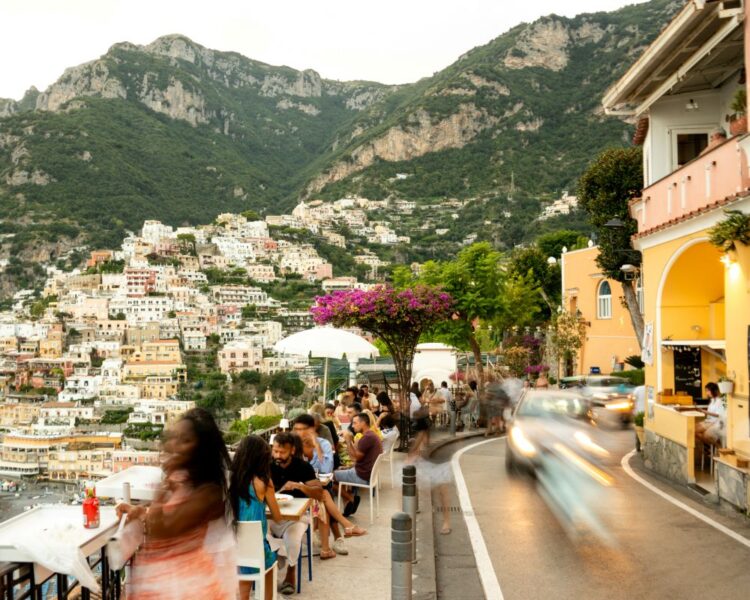 Women dining on a terrace in Positano on a luxury girlfriend trip around the world, with the Amalfi Coast hillside in the background.