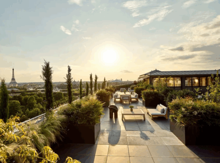 Sunset view from a rooftop terrace with seating and greenery overlooking Paris
