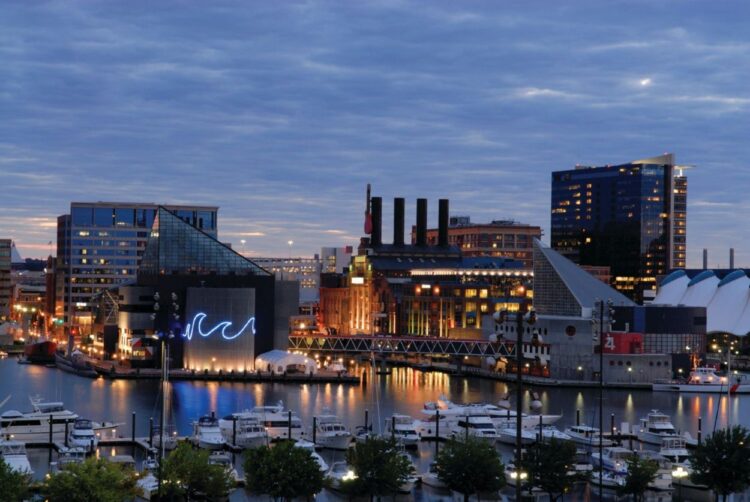 View of Baltimore’s Inner Harbor at dusk featuring the iconic Four Seasons Hotel, luxury yachts, and the National Aquarium – a perfect setting for a luxury family vacation.
