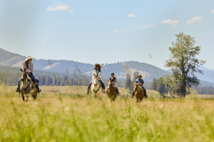 Family riding horses through a grassy meadow at Paws Up