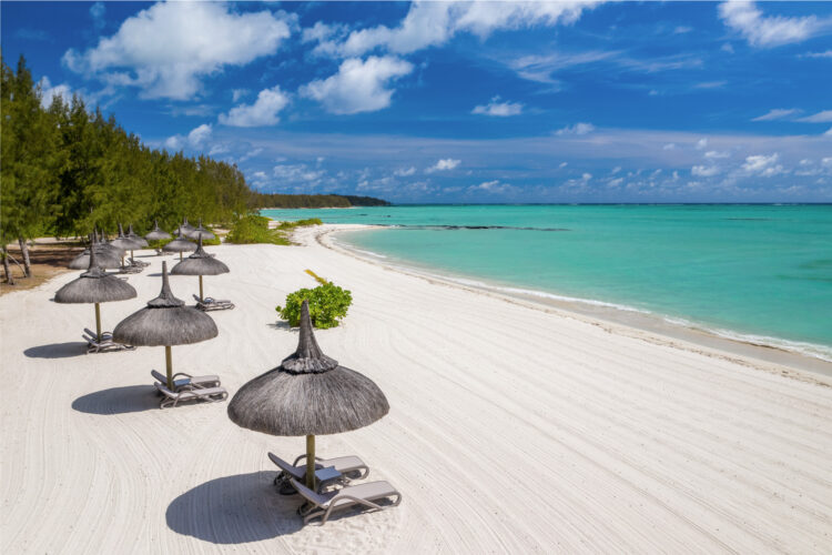 Thatched umbrellas and lounge chairs lined up along a white-sand beach with turquoise water