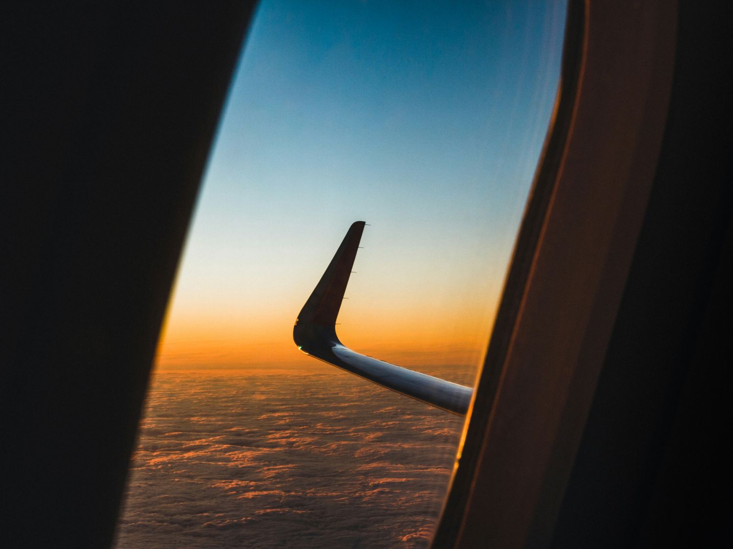 Airplane wing above clouds at sunset, symbolizing a seamless luxury around-the-world journey