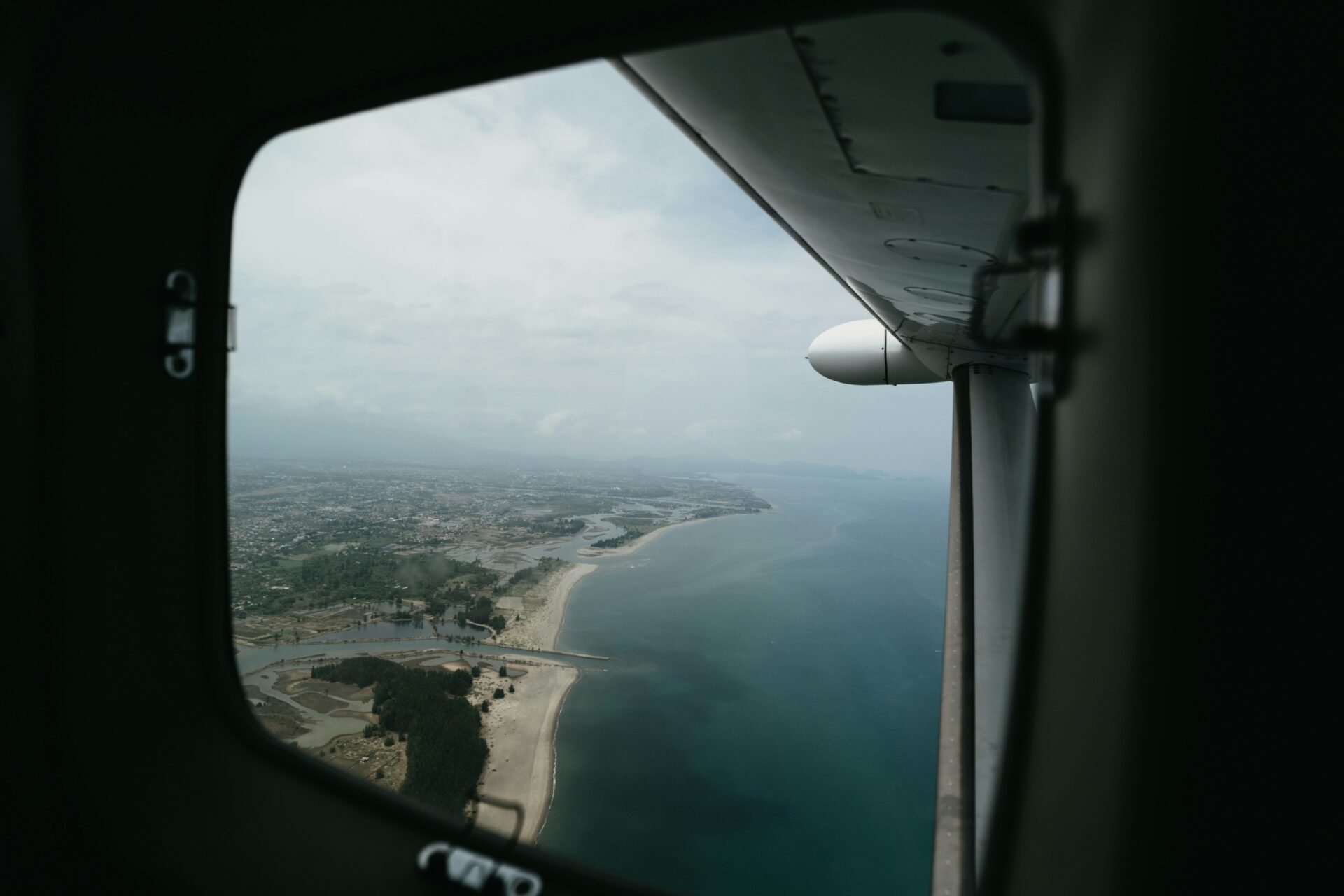 Aerial view from a private aircraft window flying over a coastal destination during a luxury around-the-world journey