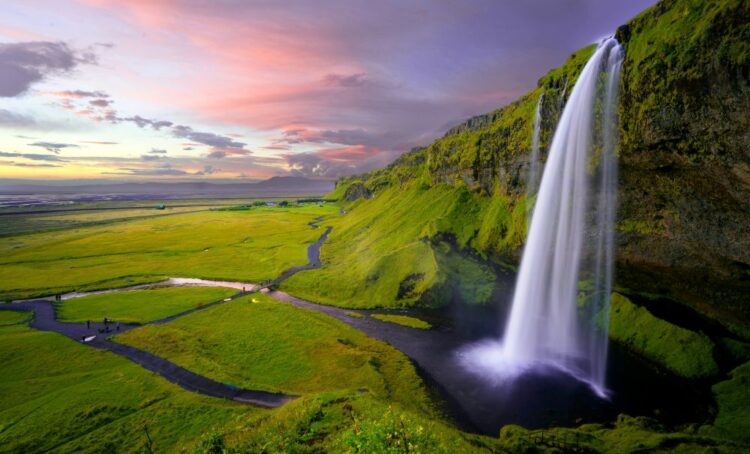 Waterfall in Iceland’s green summer landscape, one of the best places to travel in July