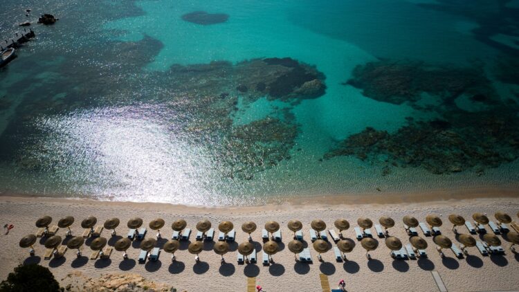 Aerial view of Romazzino's private white-sand beach with thatched umbrellas on Sardinia's Costa Smeralda